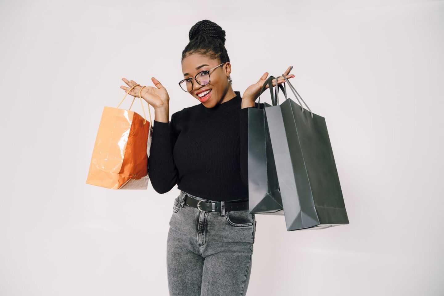 Black Woman holding one shopping back in her right hand and two in her left hand.