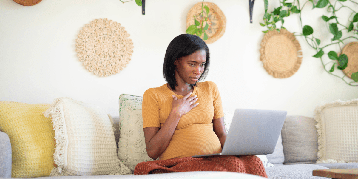 Black woman who is pregnant looking at a computer in disbelief. This image is a blog post banner about baby registry regrets