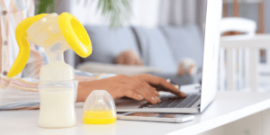 Image of a working mom on her computer with her breast pump on her desk. This image is for the blog post breast pumps for moms on the go