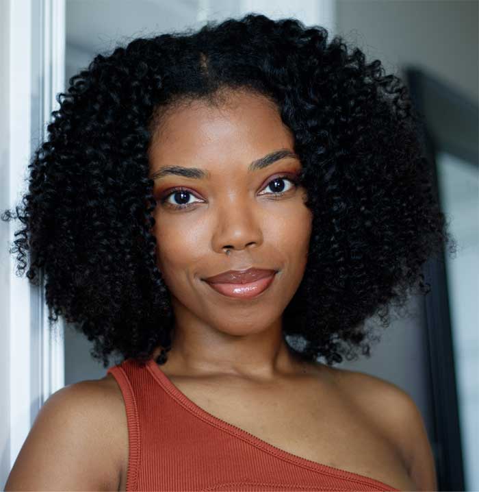 Image of Black woman with naturally curly hair wearing a one sleeved peach colored shirt. This image is for the blog post SoDazzling Instagram Link in Bio