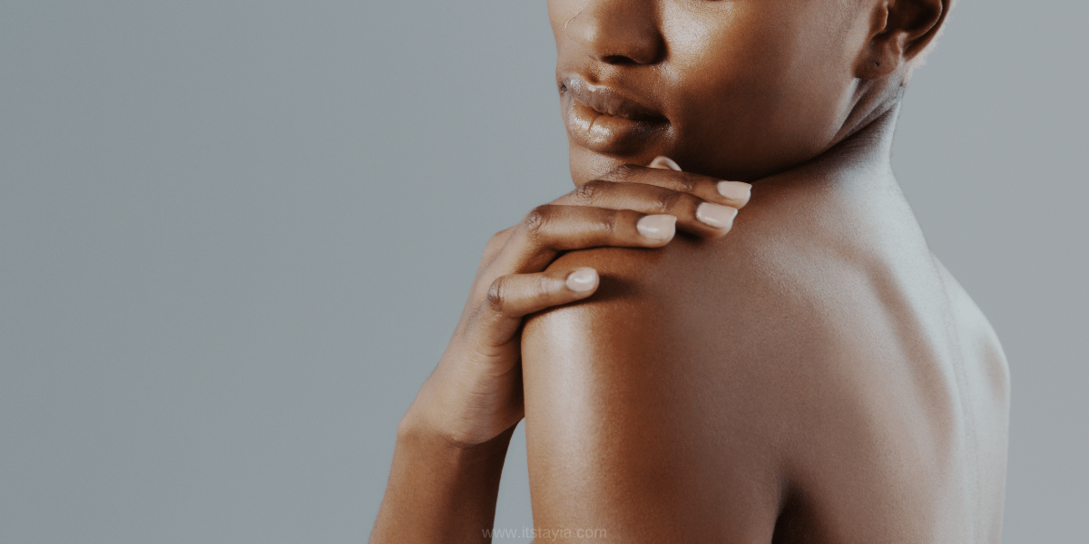 Black woman with hand right hand on her left shoulder showing her glowing skin. This is a banner for a blog post about building a body care routine and body care products