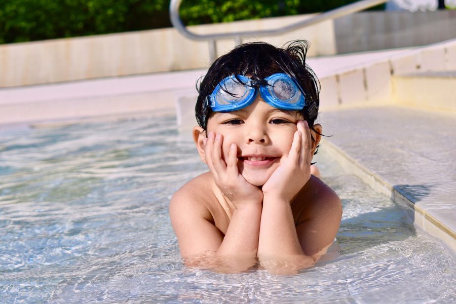 smiling toddler wearing swim goggles while sitting in swimming pool